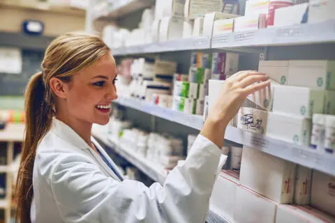 Happy woman, pharmacist or reading medicine for stock check at pharmacy for pills information. Healthcare, medical internship or girl by shelf for pharmaceutical drugs for boxes or product inventory