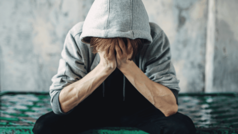 Man with opioid addiction sitting on park bench with head in his hands