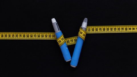 Two Ozempic injection pens wrapped in a yellow measuring tape