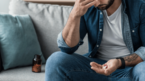 Man sitting on a couch holding pills