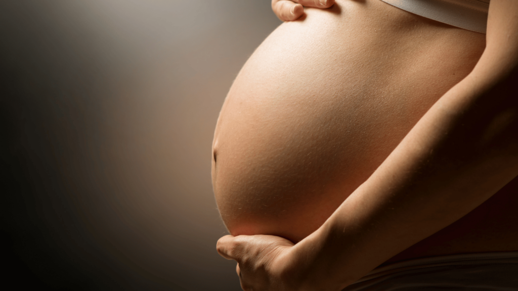 Close-up of a pregnant belly with hands gently cradling it, symbolizing maternal health and opioid use disorder (OUD) management during pregnancy and postpartum with Suboxone