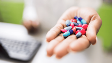 Close-up of a hand holding various colorful prescription pills, highlighting the risks of opioid addiction even when taken as prescribed