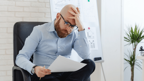 Stressed man in an office holding his head while reviewing documents, symbolizing the emotional and psychological triggers that can lead to opioid relapse