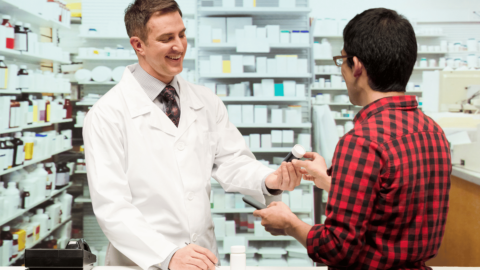 Pharmacist handing a prescription bottle to a patient at a pharmacy counter, representing the discussion on whether Suboxone should be taken daily or as needed (PRN) for opioid addiction treatment