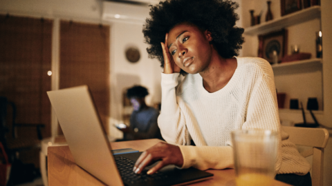 Woman sitting at a desk, looking fatigued and overwhelmed while using a laptop, representing the early warning signs of relapse and the importance of recognizing emotional and behavioral triggers