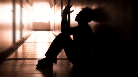 Silhouette of a person sitting against a wall in a dimly lit hallway, symbolizing the effects of Suboxone, its role in opioid addiction treatment, and the reality of buprenorphine’s impact on euphoria