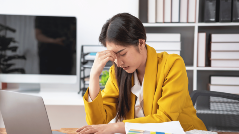 Frustrated woman sitting at her desk, holding her forehead in distress, representing ongoing cravings while on Suboxone and the challenges of medication-assisted treatment