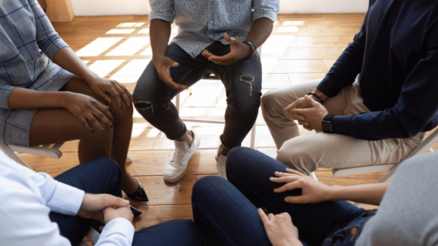 Group therapy session with people sitting in a circle, discussing opioid addiction treatment options, including at-home recovery alternatives