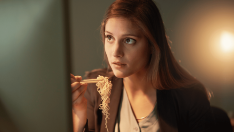 Woman eating noodles while working on a computer, representing the impact of food on Suboxone absorption and whether it should be taken on an empty stomach