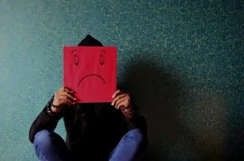 Person holding a red unhappy face up to their head in need of the best antidepressant for treating depression