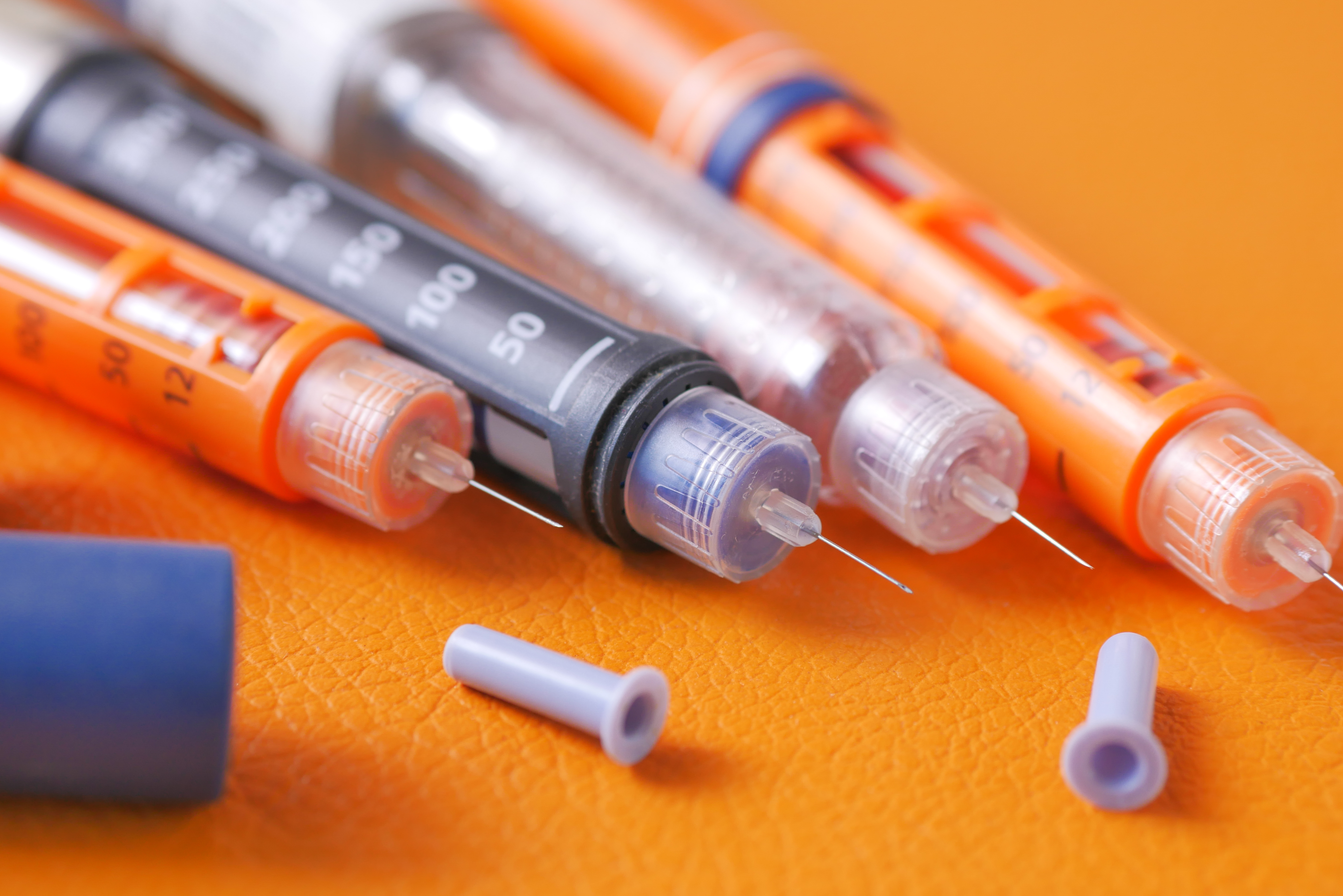 Insulin pens on orange background, close up