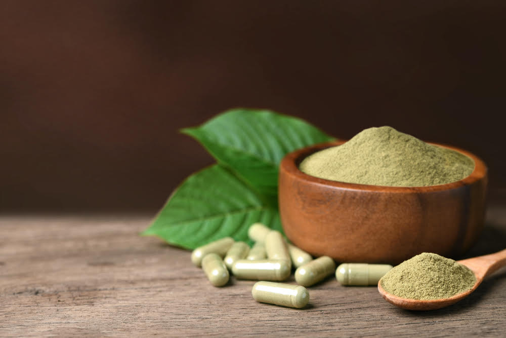 Kratom powder in a wooden bowl next to Kratom capsules used for stimulant and opioid-like effects in pain management and opioid withdrawal treatment